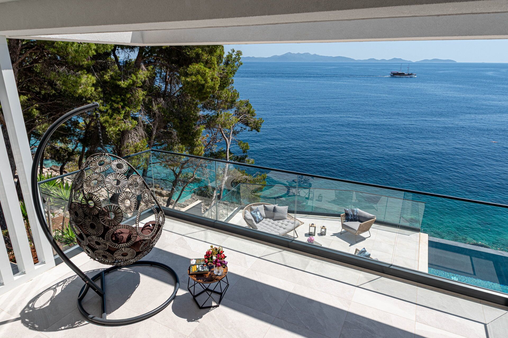 A balcony with a glass railing overlooking a pool and the sea.