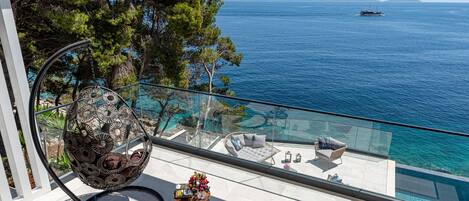 A balcony with a glass railing overlooking a pool and the sea.