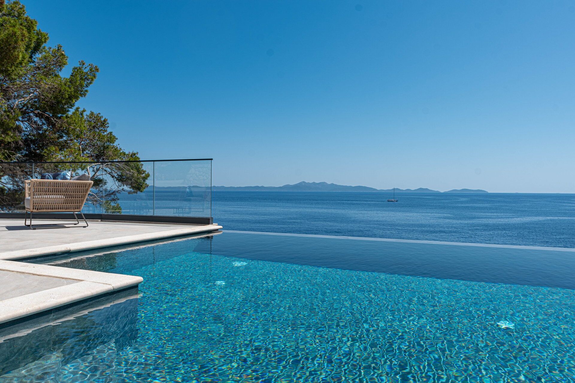 Una piscina infinita de color azul cristalino, con vistas al mar y montañas lejanas.