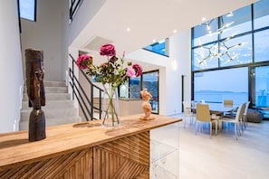 A modern interior with a wooden reception desk, a staircase, and a dining area with a view.