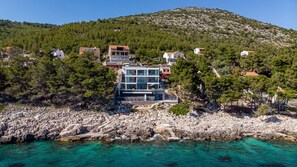 A coastal property with a modern two-story building, rocky shoreline, and clear turquoise waters.