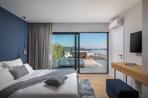 Et moderne soveværelse med en stor seng, et skrivebord og udsigt til en balkon med swimmingpool og bjerge.