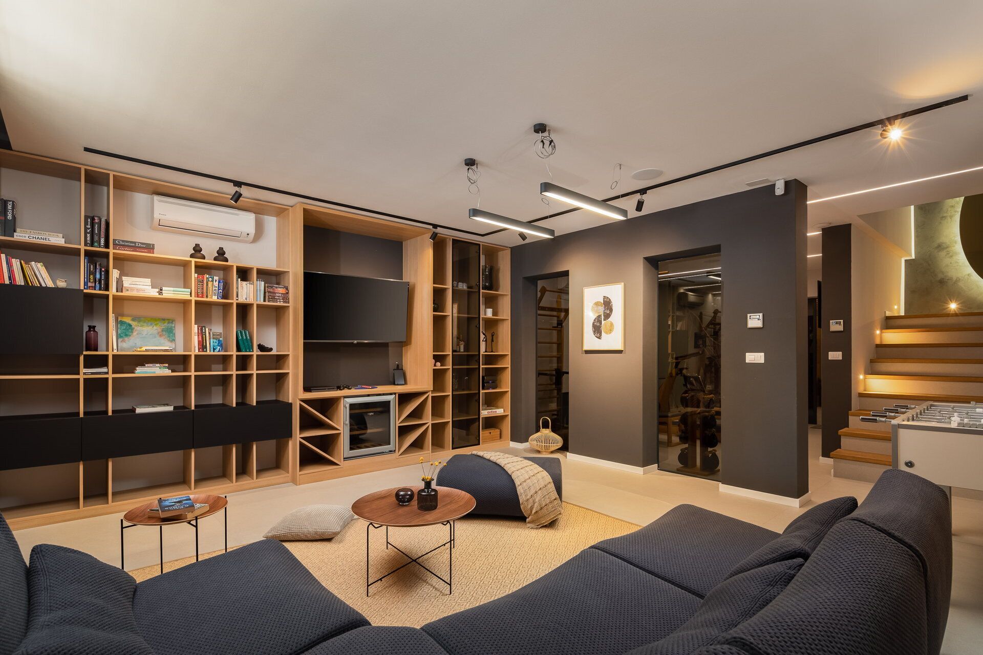 Un salon moderne doté d’une grande bibliothèque, d’un téléviseur à écran plat et d’un coin salon confortable avec des canapés et une table basse.