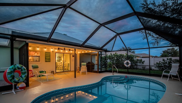 Une piscine entourée d’une structure en verre, avec des chaises longues et un patio couvert.
