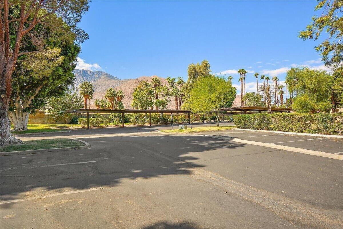 A parking lot with a covered pedestrian bridge, trees, and a mountain in the background.