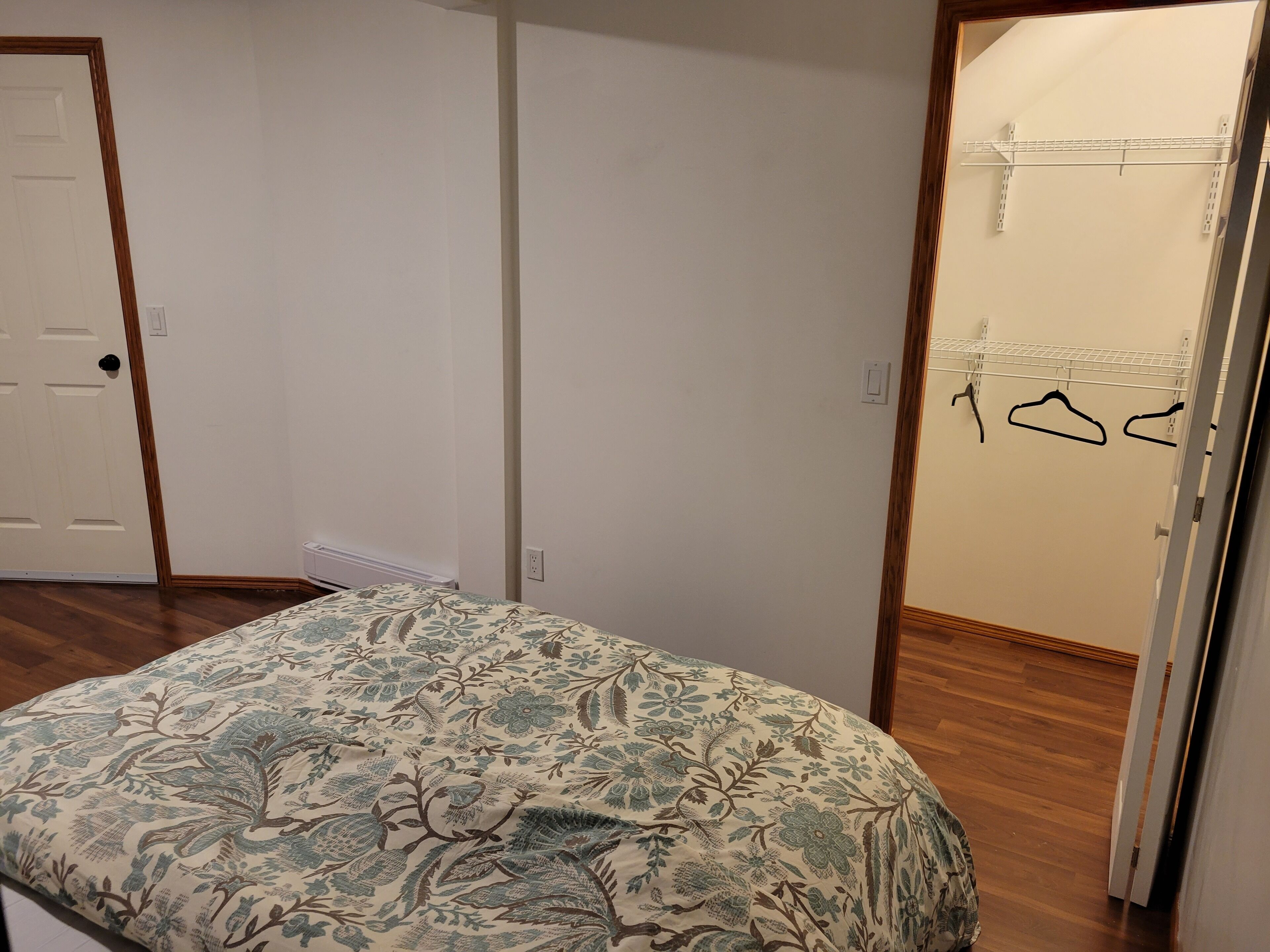 Un dormitori amb un llit, una porta i un armari amb penjalls.