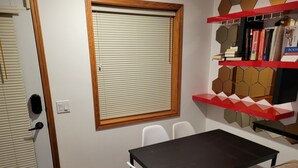 Una habitación con puerta de madera, una ventana con persianas, una mesa con sillas y una estantería con libros.