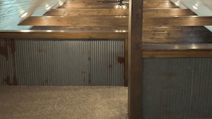 An attic space with wooden beams, a metal ceiling, and a visible ceiling fan.