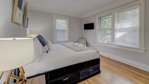 Un dormitorio con una cama, una silla, un televisor y dos ventanas con persianas.