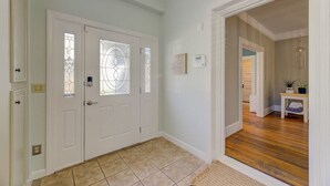 Un pasillo con una puerta blanca de paneles de vidrio, suelo de baldosas y suelo de madera que conduce a otra habitación.