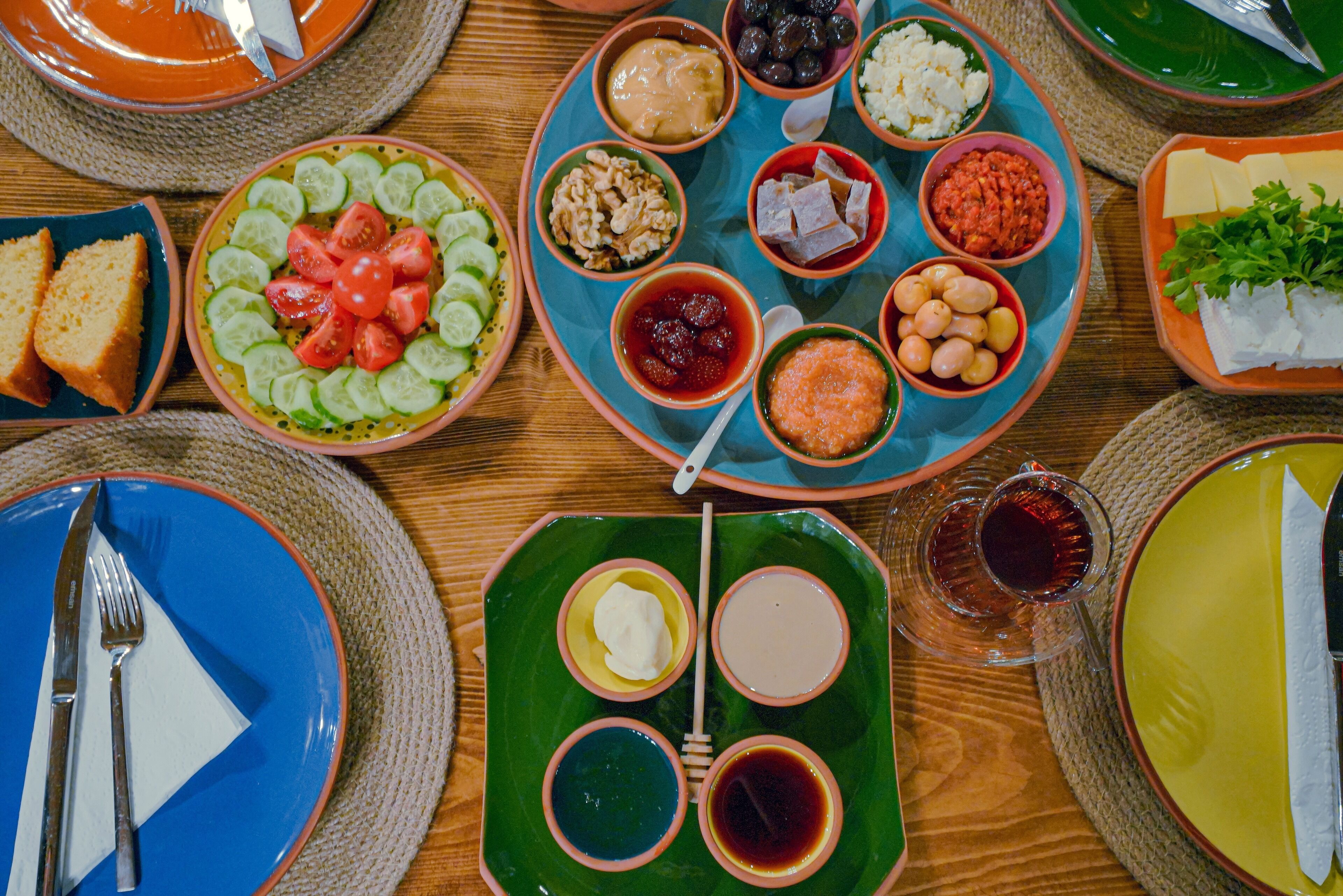 A table with various dishes and condiments, including sliced cucumbers, tomatoes, and different types of cheese and nuts.