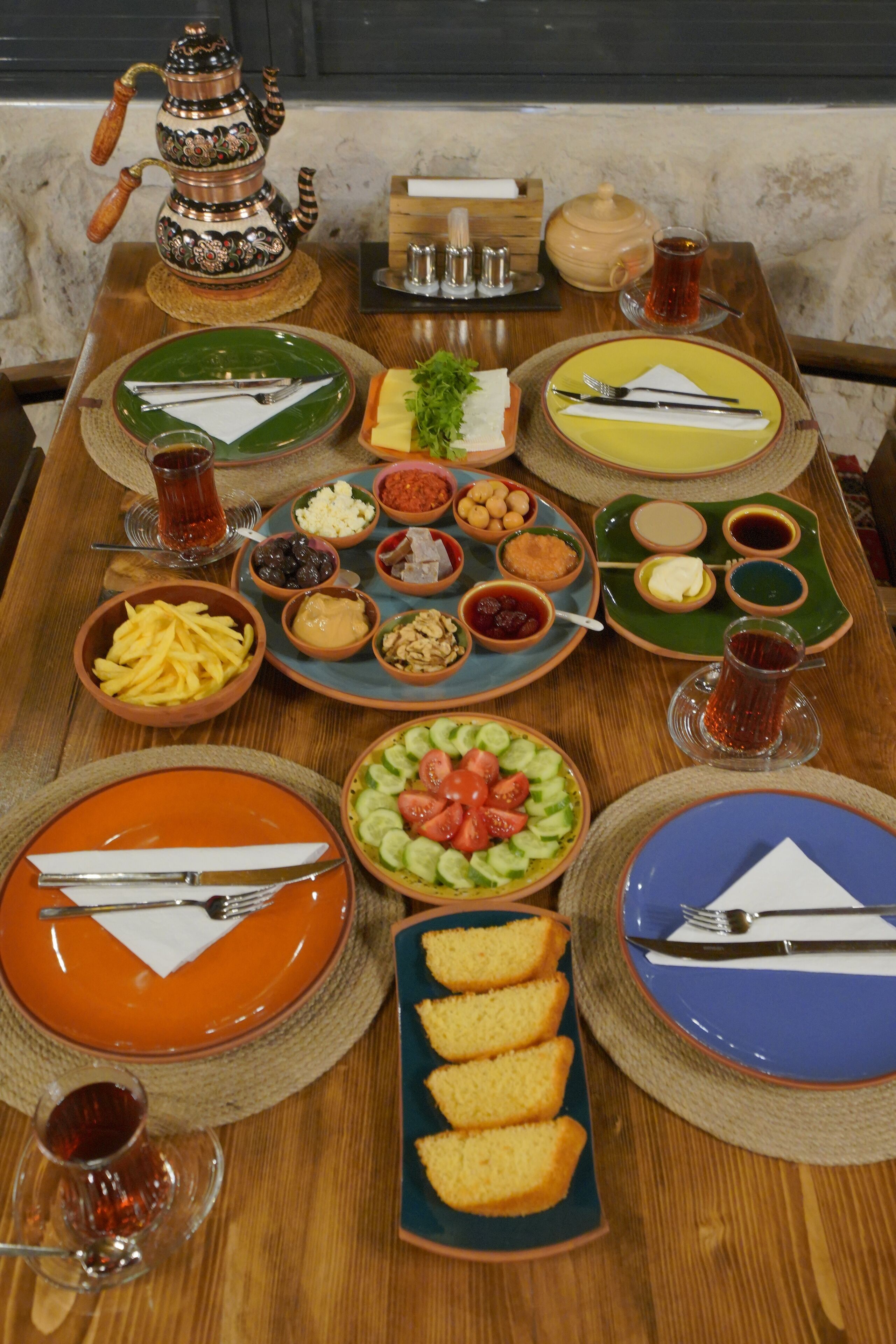 A table set with various dishes, including a bowl of fries, a plate of sliced cucumbers and tomatoes, and a plate of bread.