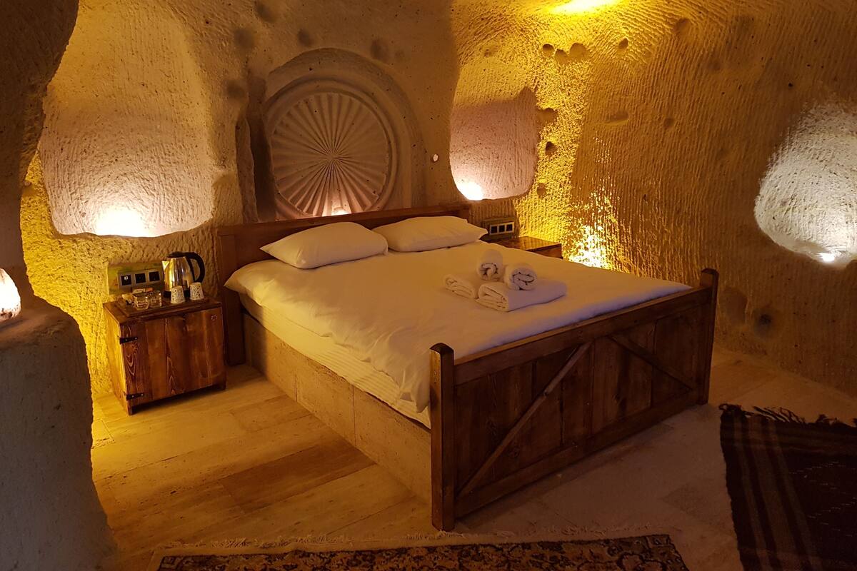 A cozy, rustic bedroom with a wooden bed, a round wall decoration, and a nightstand with a kettle and glasses.