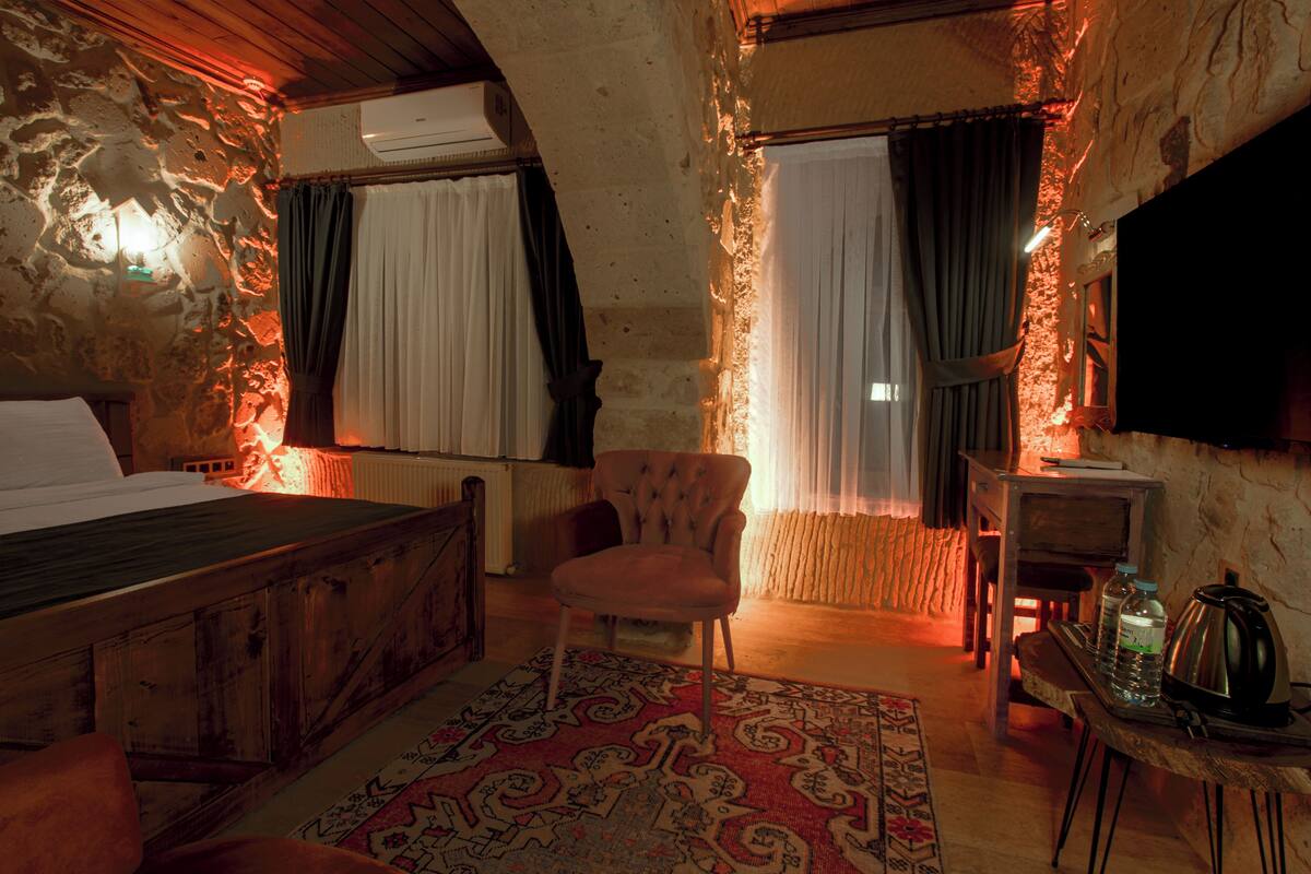A rustic room with a bed, a chair, a table with a kettle, and a TV.