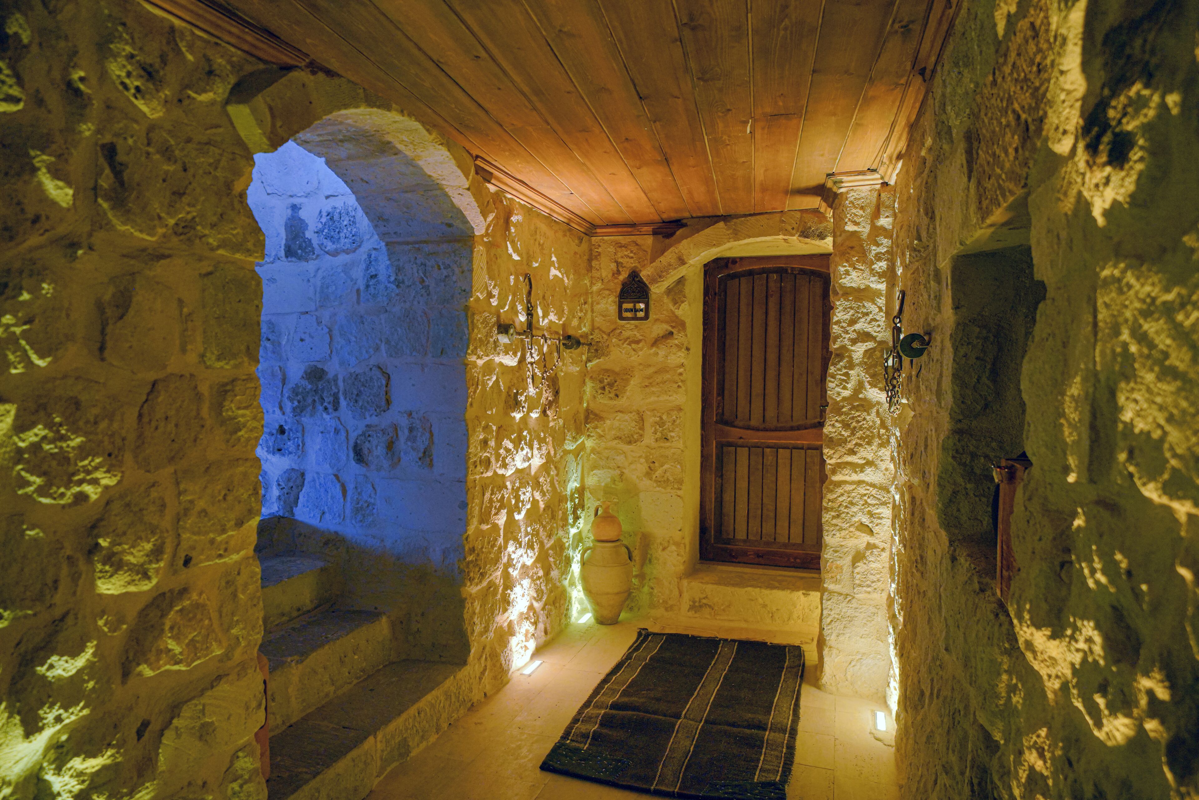 A stone-walled room with a wooden door, a small window, and a rug on the floor.