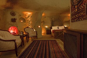 A cozy interior with a fireplace, a sofa, a bed, and a patterned rug. - Babili Cappadocia Cave Hotel (Nevsehir)