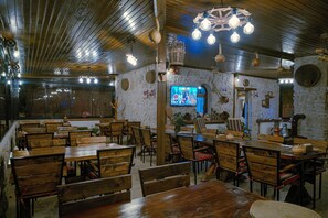 A restaurant with wooden tables and chairs, a television screen, and various decorative items on the walls. - Babili Cappadocia Cave Hotel (Nevsehir)