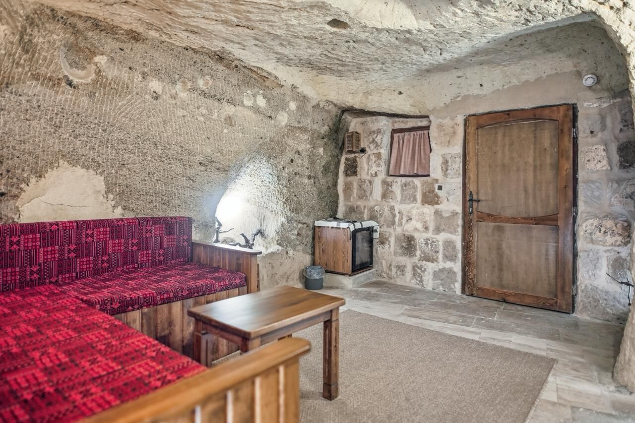 A stone-walled room with a red patterned sofa, a wooden table, a fireplace, and a wooden door.