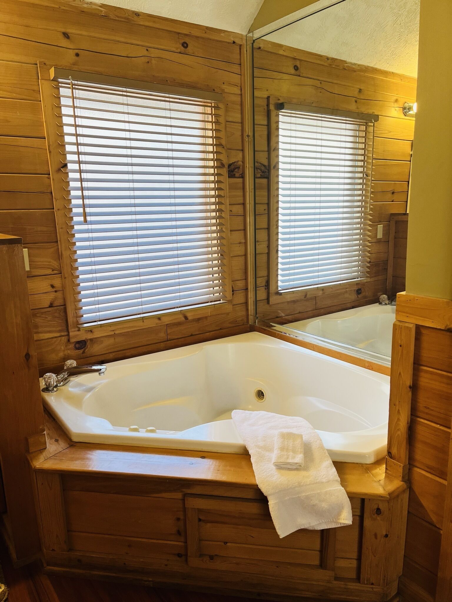 A wooden cabin bathroom with a large bathtub, wooden walls, and a mirror above the tub.