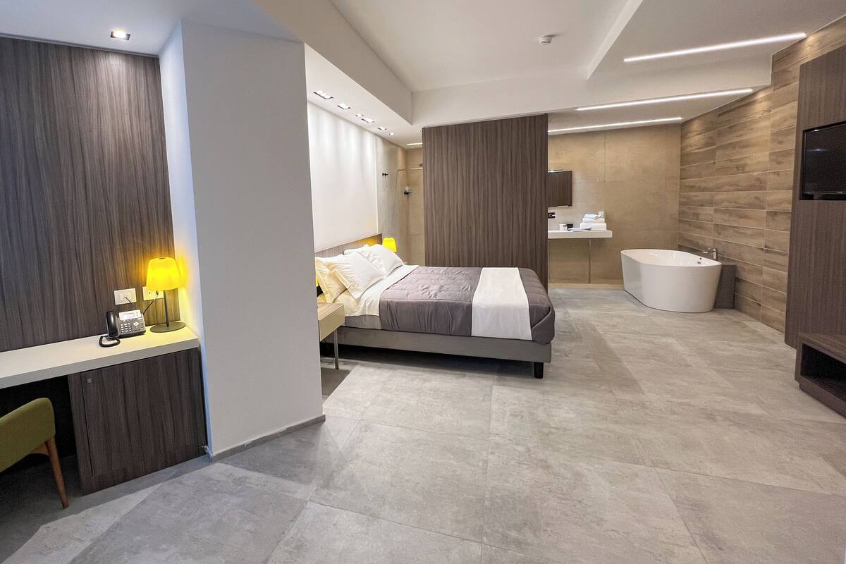 A modern hotel room with a bed, desk, and a large bathtub.