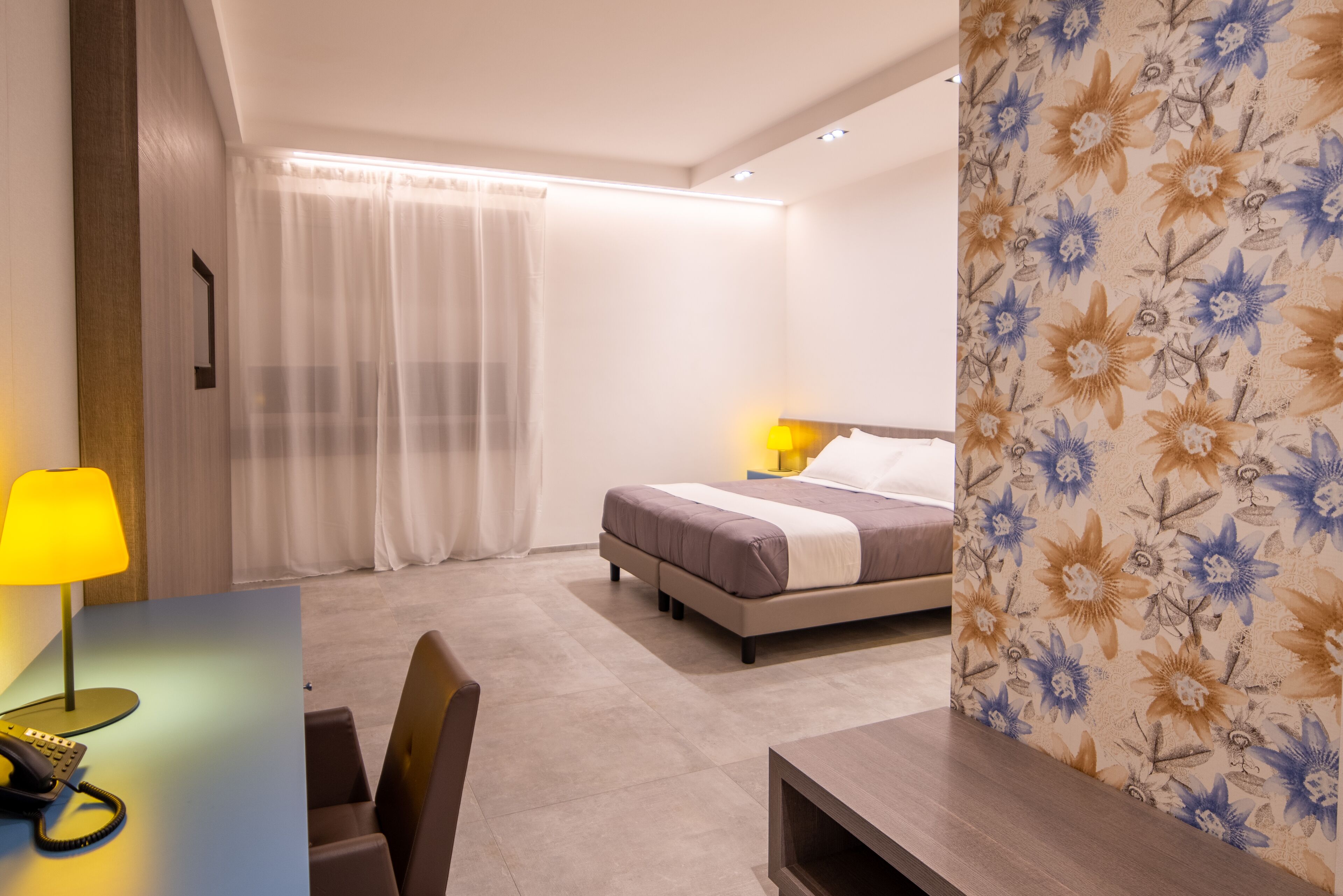 A hotel room with a bed, a desk with a lamp, and a chair.