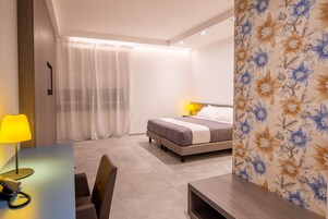 A hotel room with a bed, a desk with a lamp, and a chair.