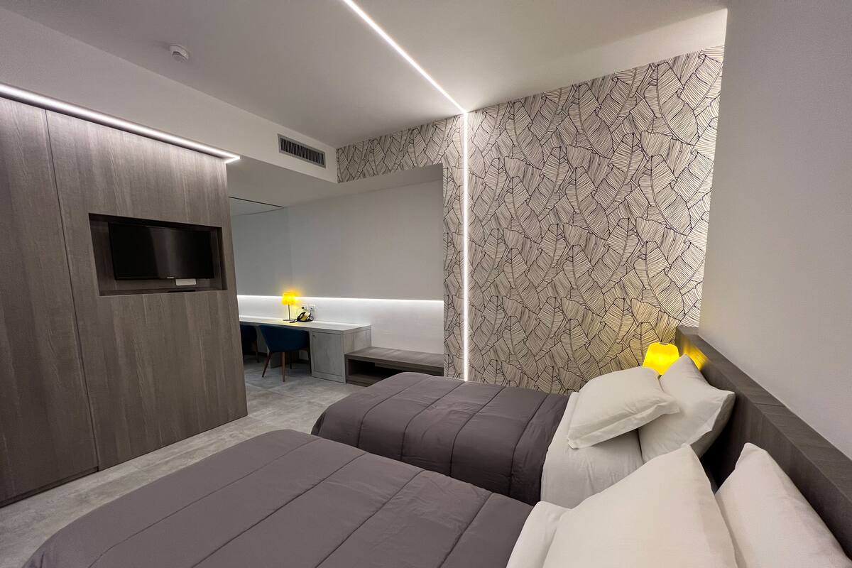 A modern hotel room with two beds, a desk, and a TV.