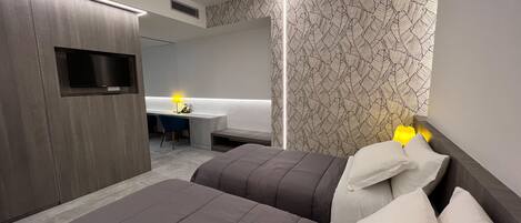 A modern hotel room with two beds, a desk, and a TV.
