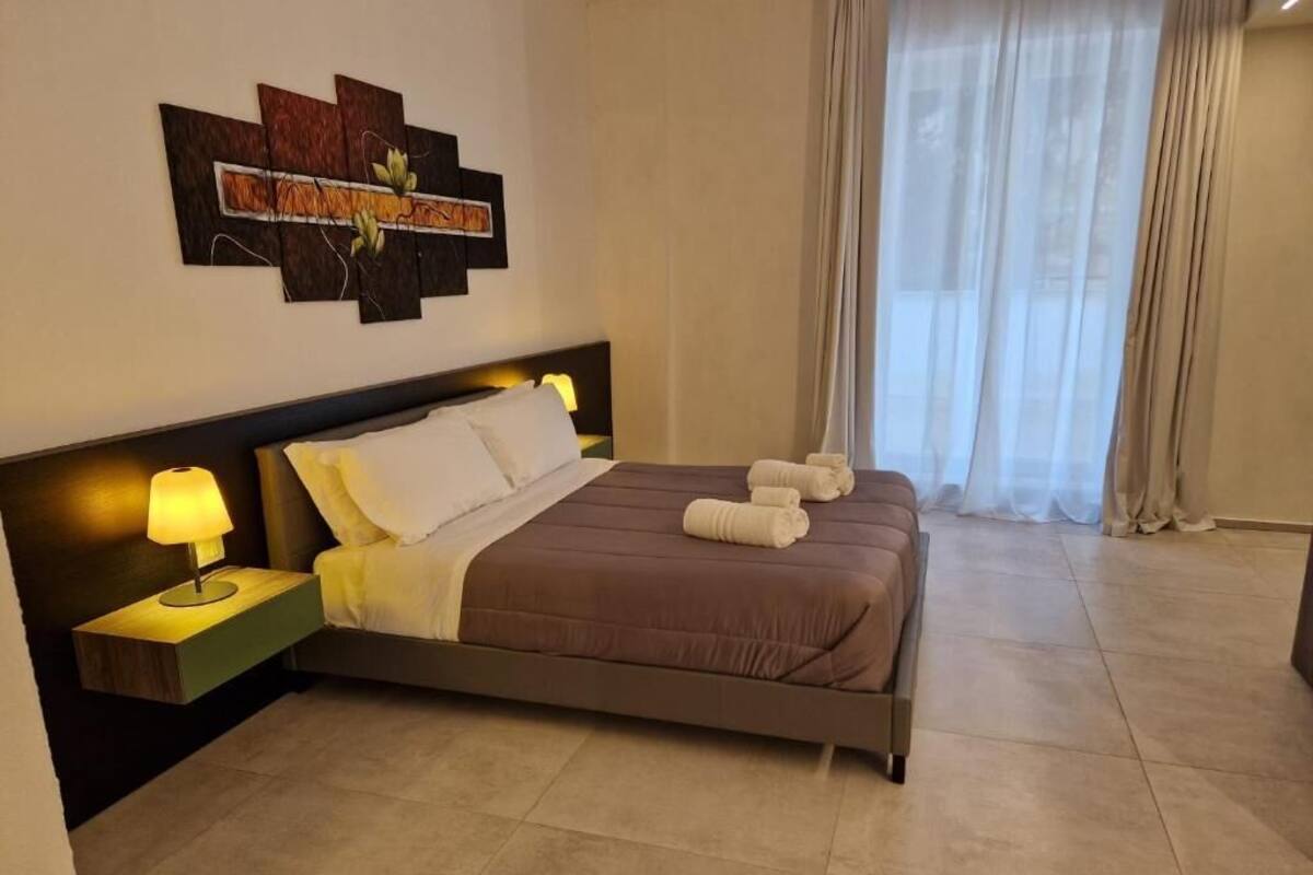 A neatly made bed with a brown bedspread and white pillows, a bedside table with a lamp, and a wall art piece above the bed.