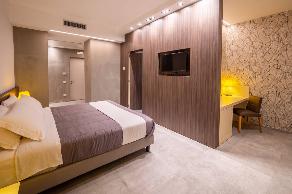 A modern bedroom with a large bed, a desk, and a TV.