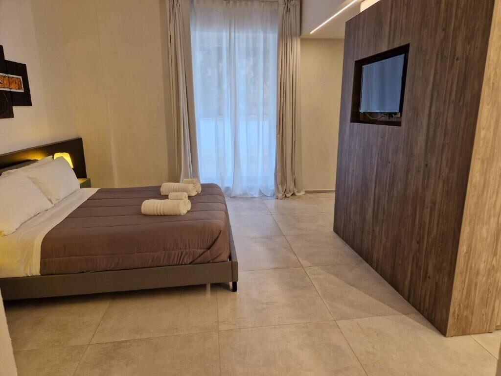 A hotel room with a bed, a TV mounted on a wooden wall, and a window with curtains.