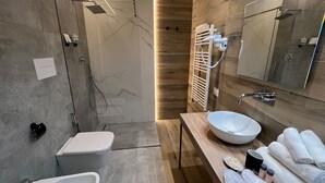 Un baño moderno con ducha envuelta en vidrio, un lavamanos blanco y un mueble de tocador de madera.