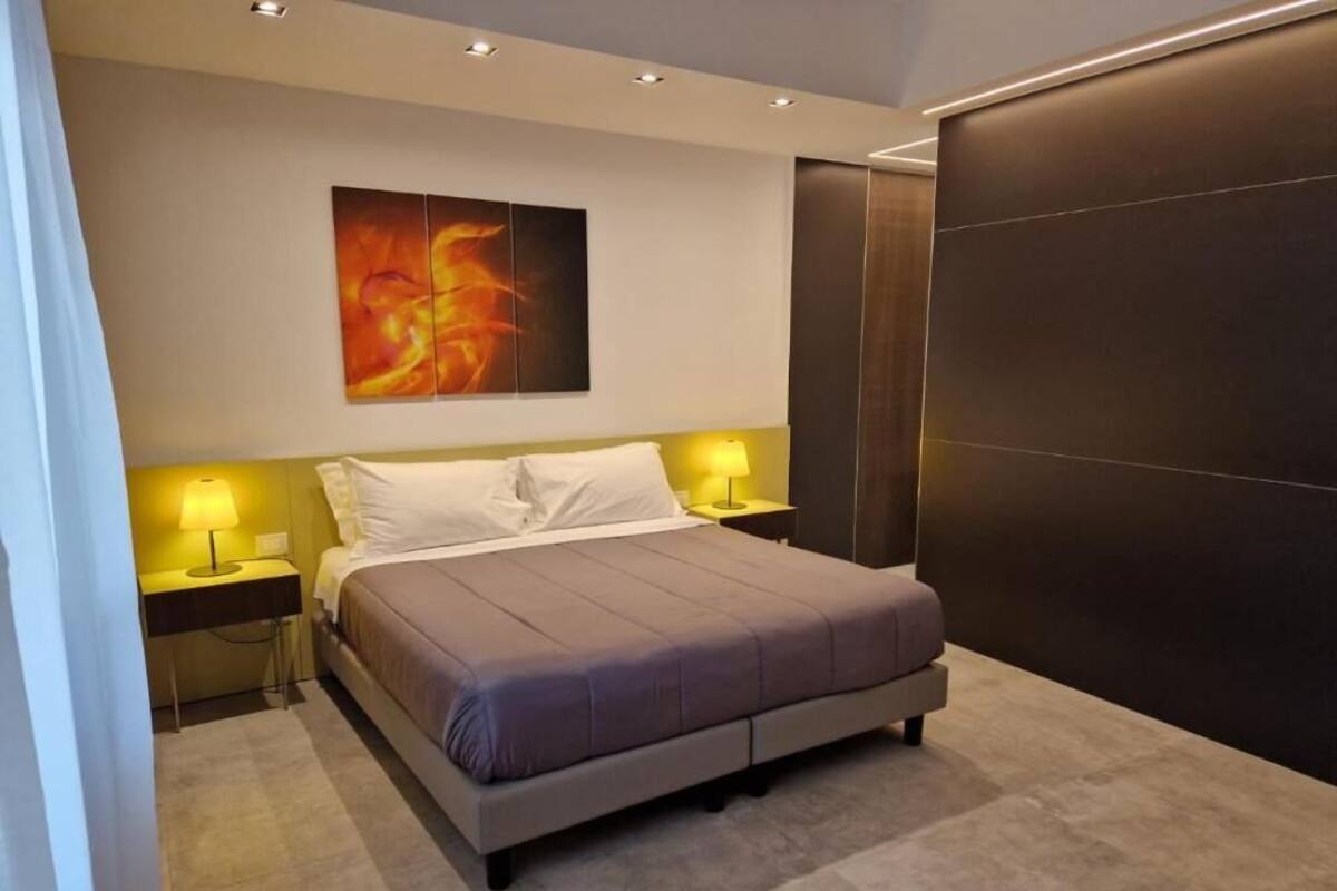 A modern bedroom with a large bed, two bedside tables with lamps, a wall-mounted artwork, and a dark accent wall.
