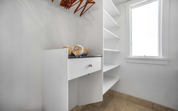 Een witte kamer met een inbouwplank en een raam, en een betegelde vloer.