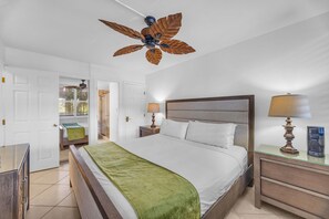 Een hotelkamer met een groot bed, een houten hoofdbord, twee nachtkastjes met lampen, een plafondventilator en uitzicht op een balkon.