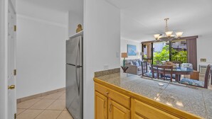 Eine Küche mit Granit Arbeitsplatte, Holzschränken und einem Edelstahlkühlschrank. Ein Essbereich mit Tisch und Stühlen bietet Blick ins Grüne.
