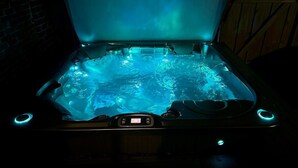Een hottub met verlichte blauwe lampjes, een bedieningspaneel en een houten wand op de achtergrond.