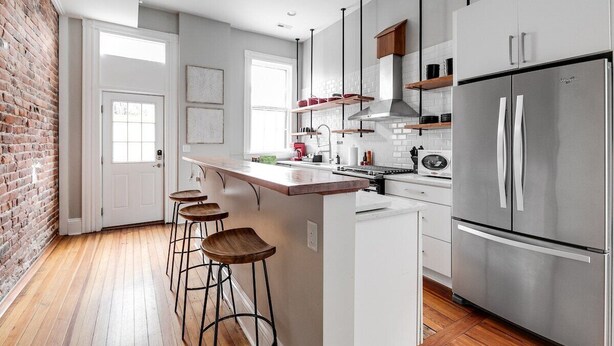 Een moderne keuken met een bakstenen muur, een groot eiland met krukken, roestvrijstalen apparatuur en een raam dat voor natuurlijk licht zorgt.