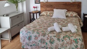 Ein ordentlich eingerichtetes Schlafzimmer mit einem hölzernen Kopfende, einer blumigen Bettdecke und einem Nachttisch mit Lampe und kleiner Pflanze.