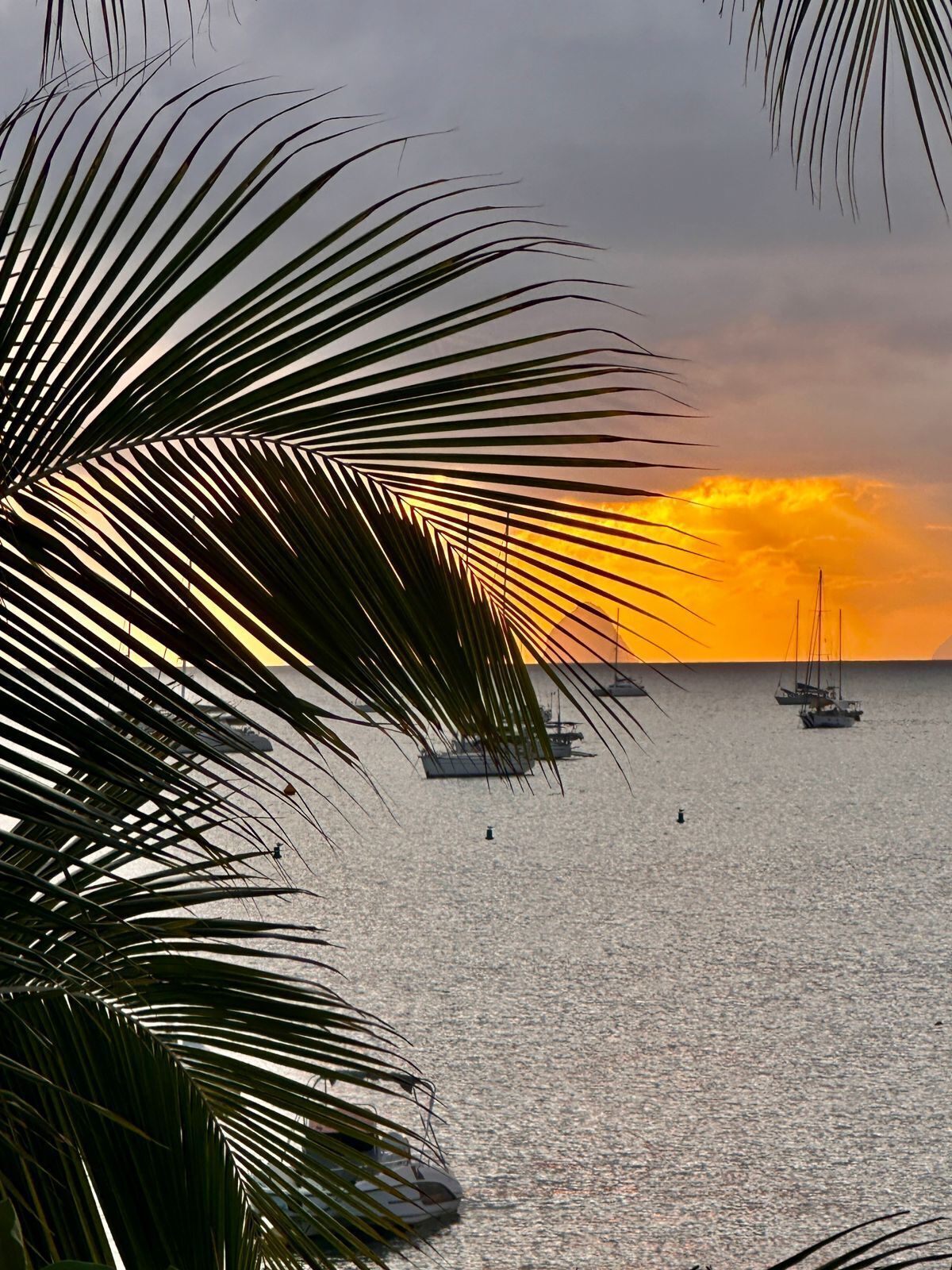 A sunset over a calm sea with sailboats.