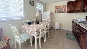 Een eethoek met een tafel voor vier personen, witte stoelen, een koelkast en een klok aan de muur.