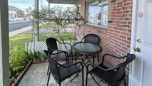 Een overdekte veranda met een bakstenen muur, een witte deur en een kleine tafel met stoelen.