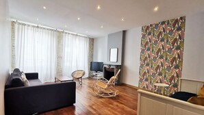 A modern living room with a sofa, a rocking chair, a television, and a fireplace. - Ô charme - 105m² apartment 15 min from Orléans (Olivet)
