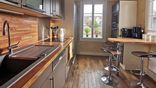 A modern kitchen with wooden countertops, stainless steel appliances, and a bar area with stools. - Ô charme - 105m² apartment 15 min from Orléans (Olivet)