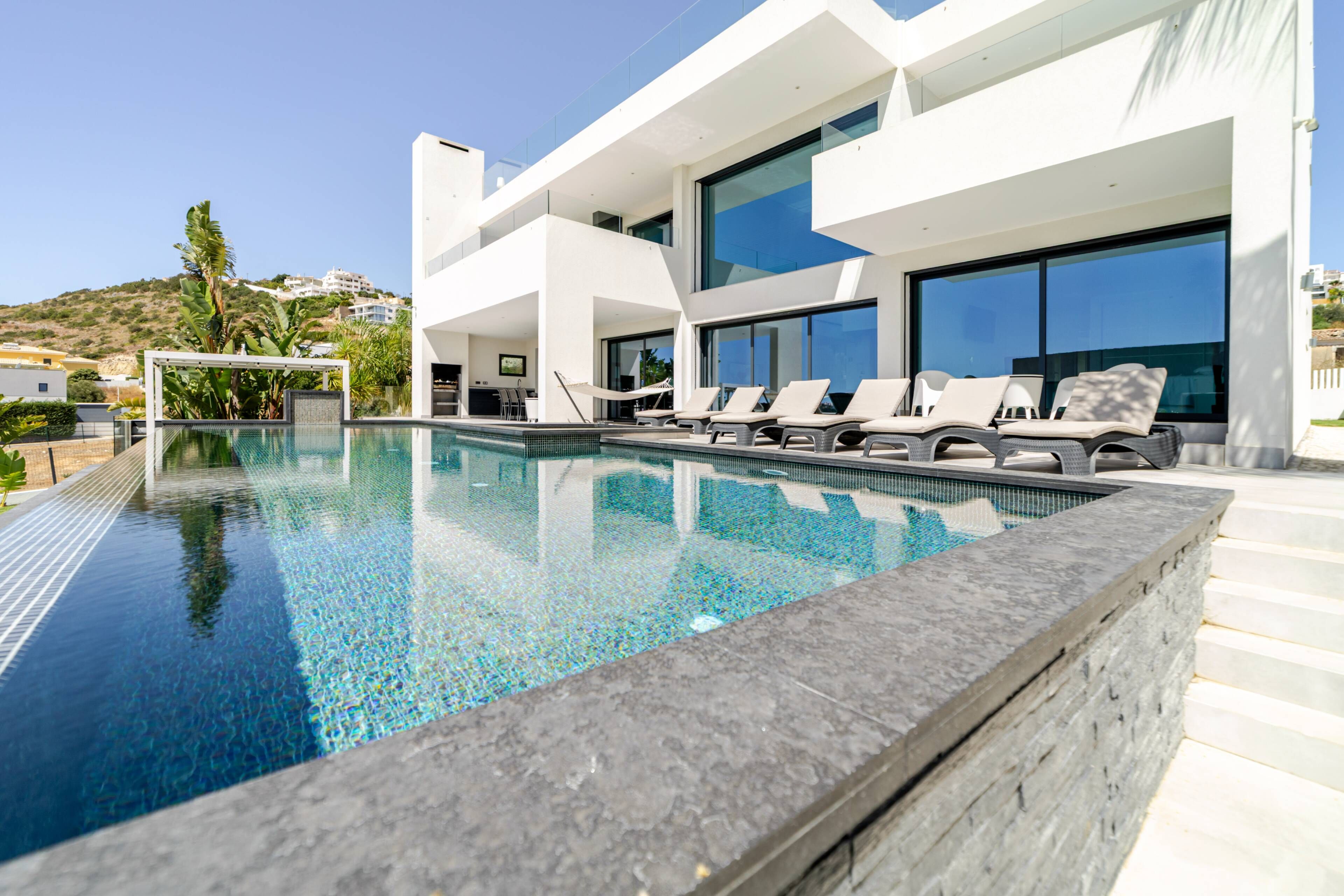 A modern pool area with a clear blue pool, lounge chairs, and a large glass facade building in the background.