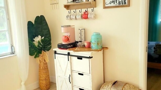 Una habitación acogedora con estación de café, una planta decorativa y un cartel que dice 'It's Summer Y'all'.