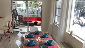 Comedor con mesa de madera para seis personas, ventilador de techo y vista a un área de estar exterior roja a través de un ventanal.