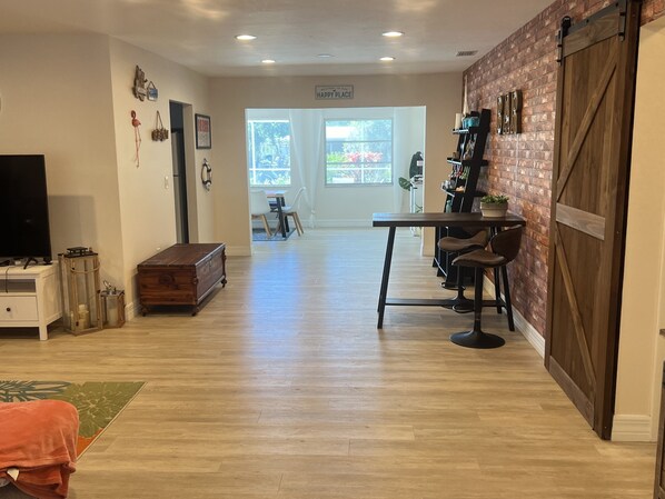 Une cuisine spacieuse avec un plancher en bois, un coin repas avec une table et des chaises, et un bar avec un mur en briques et une porte en bois.