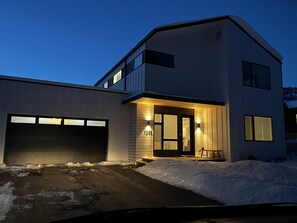 A modern two-story house with a garage, a covered porch, and a snow-covered driveway.