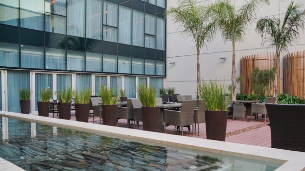 Un espace piscine extérieur moderne, avec un bord en pierre, entouré de plantes en pot et de mobilier d’extérieur.